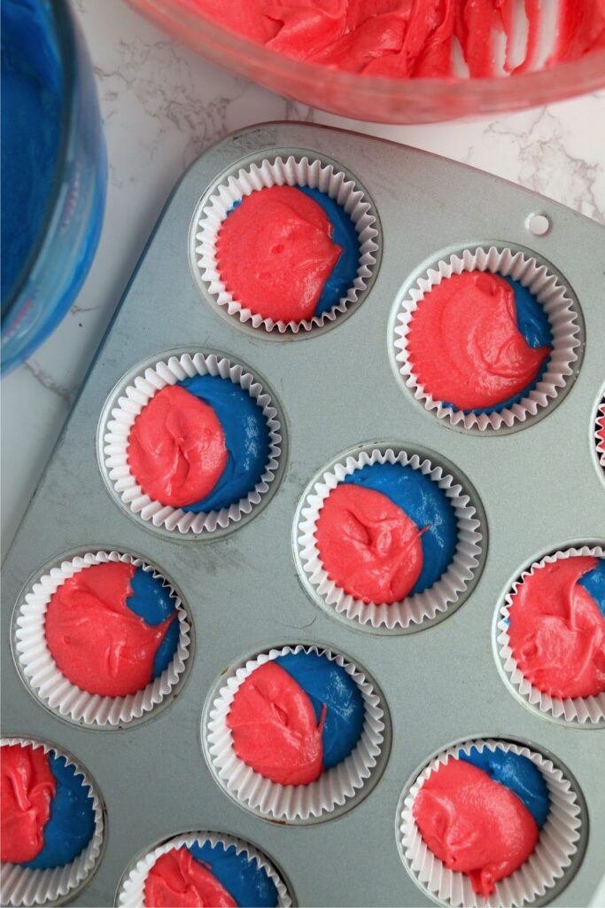 Overhead shot of red and blue-swirled cupcake batter in cupcake tins