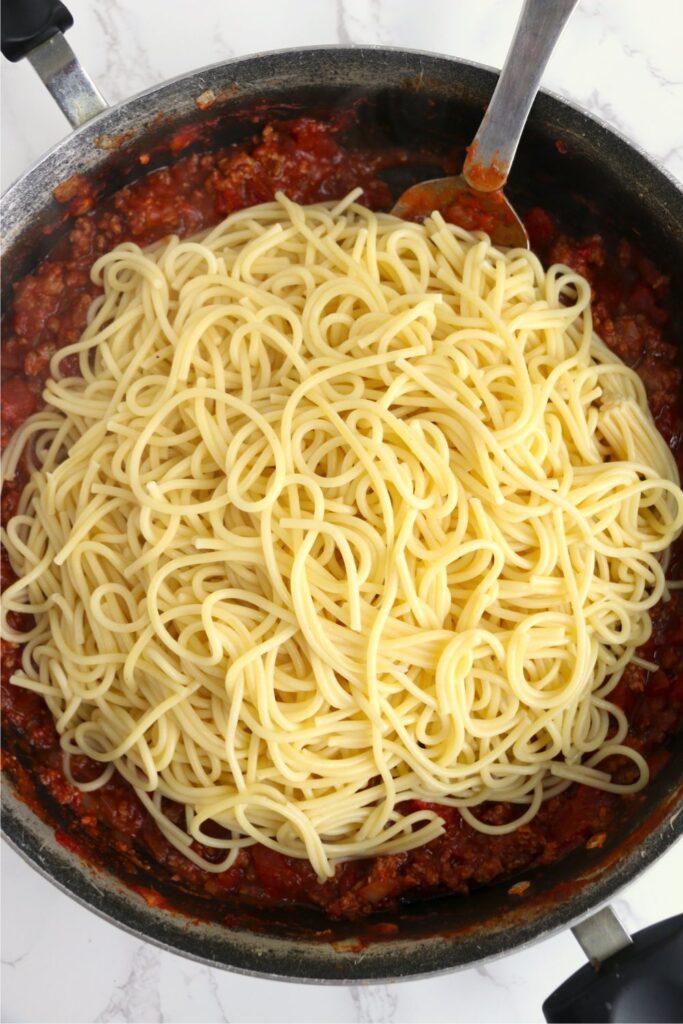 Spaghetti noodles on top of spaghetti sauce in skillet