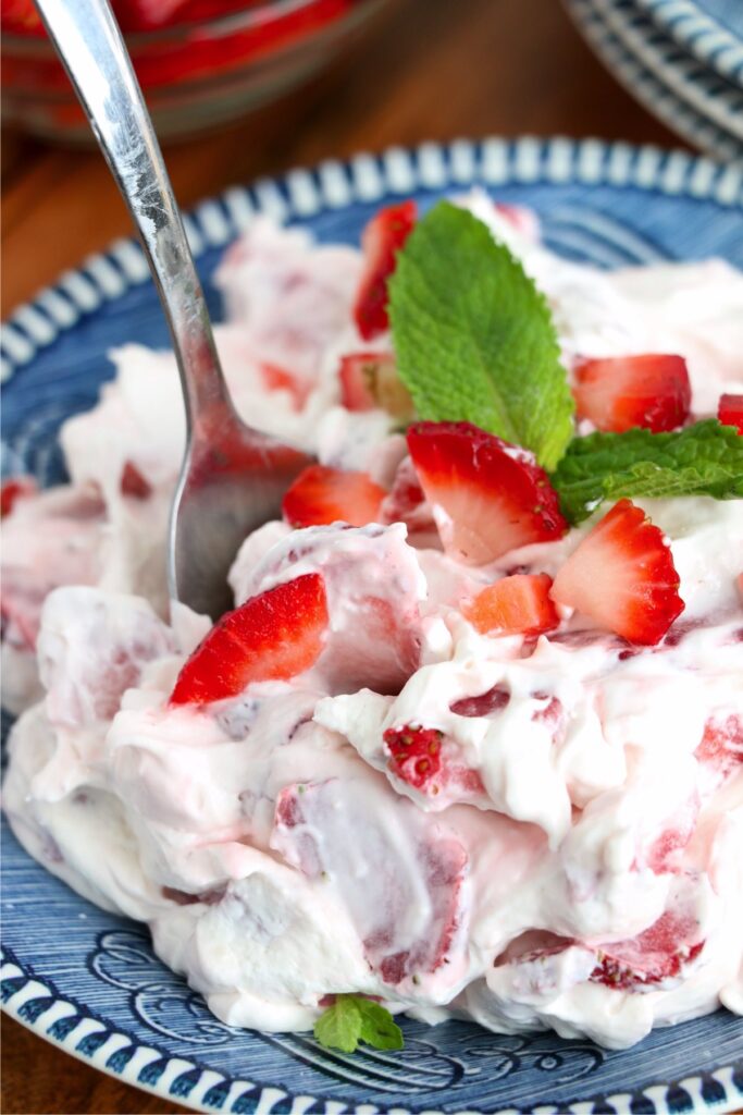 Closeup shot of spoon stuck in strawberry cheesecake salad on plate