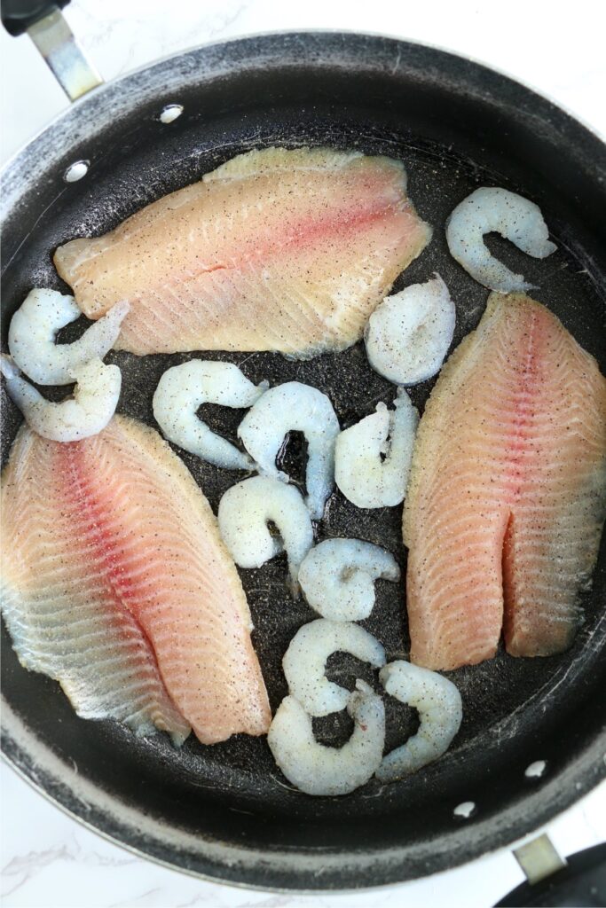 Overhead shot of raw tilapia and shrimp cooking in pan