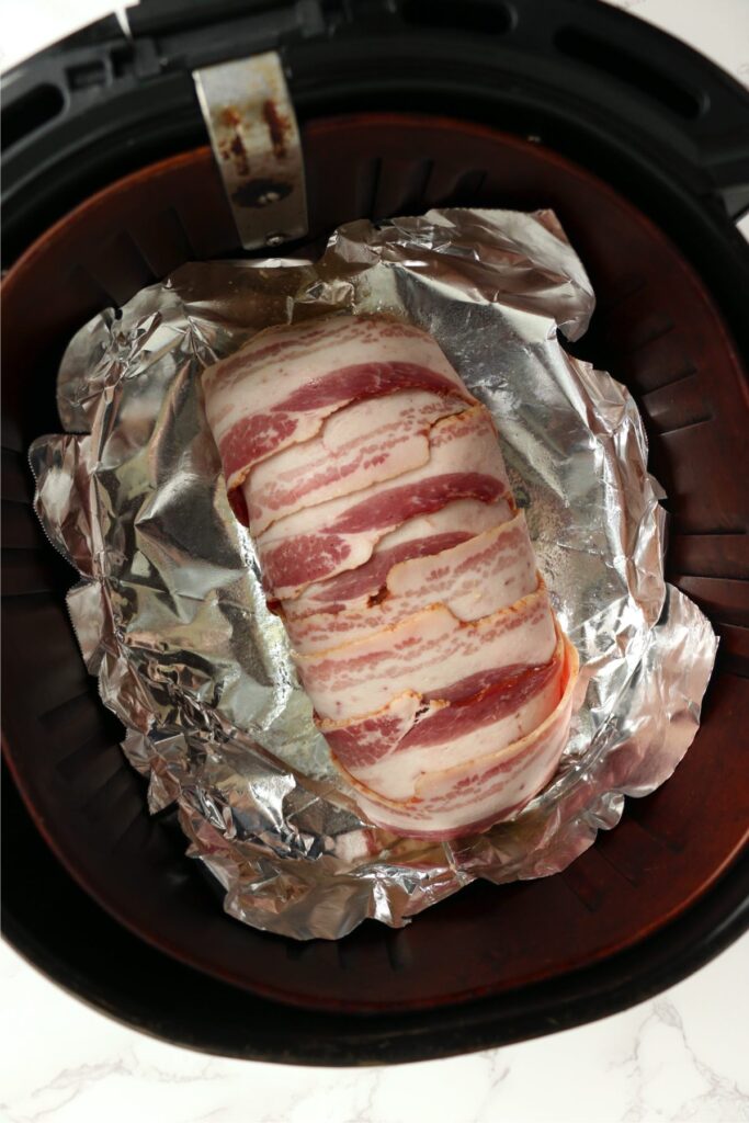 Overhead shot of bacon wrapped turkey meatloaf in air fryer basket lined with foil