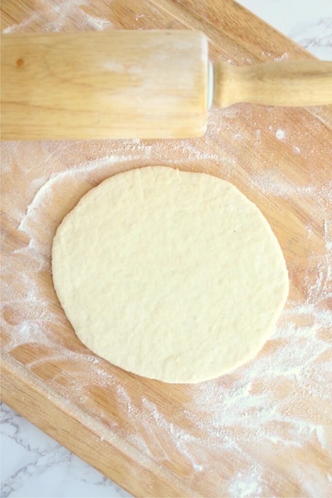 Overhead shot of flatbread dough rolled out next to rolling pin on floured cutting board