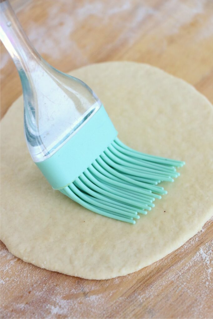 Closeup shot of oil being brushed onto flatbread dough