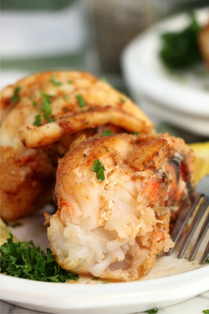 Closeup shot of butter poached lobster tail with bite taken out on plate