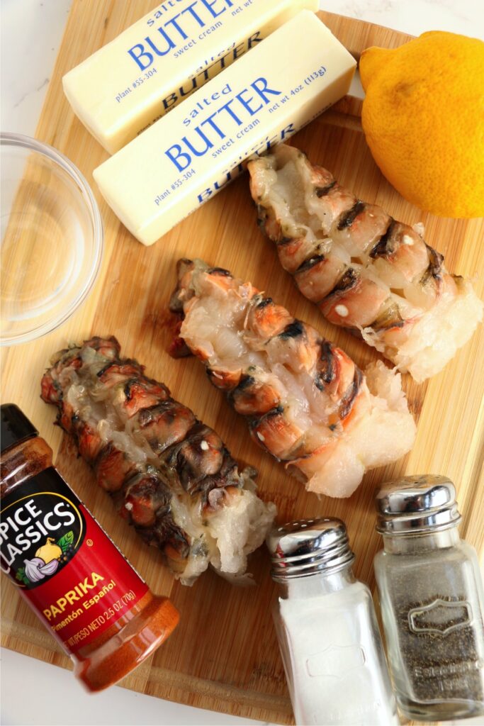 Overhead shot of raw lobster tails, butter, salt, pepper, and paprika on cutting board