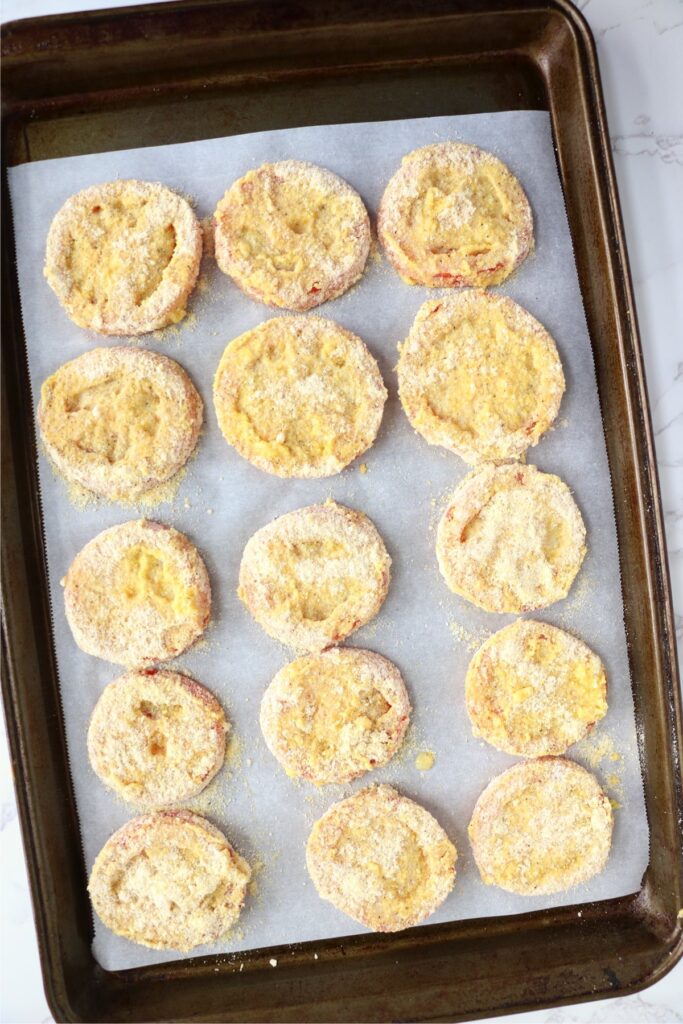 Overhead shot of coated tomato slices on baking sheet lined with parchment paper