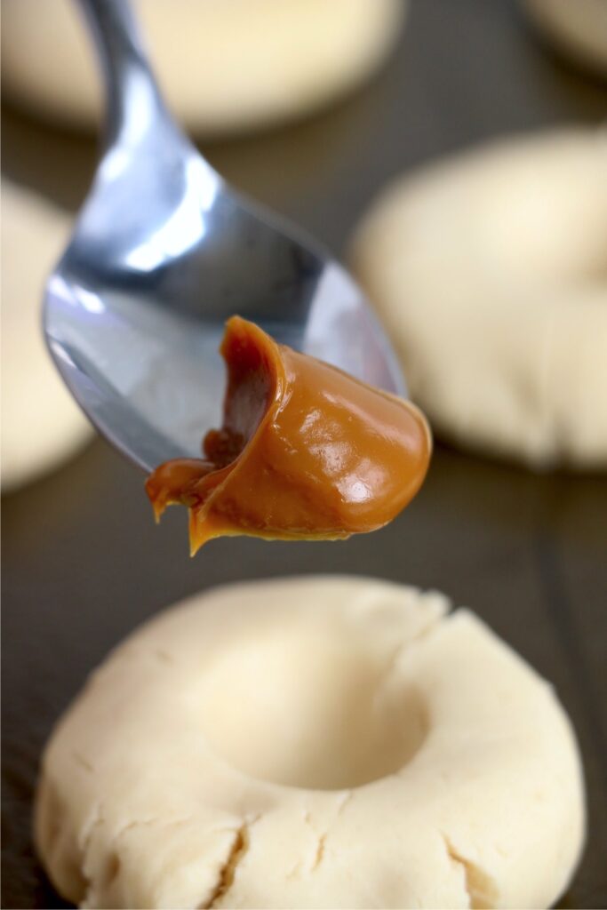 Closeup shot of spoonful of dulce de leche over cookie dough with depression