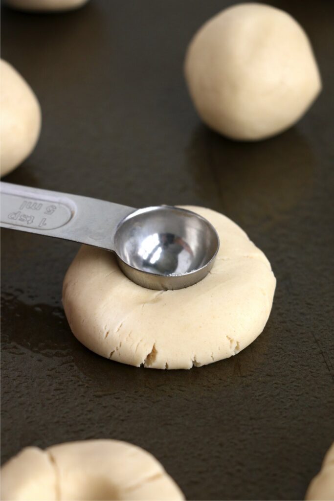 Closeup shot of measuring spoon pressing divot into center of cookie