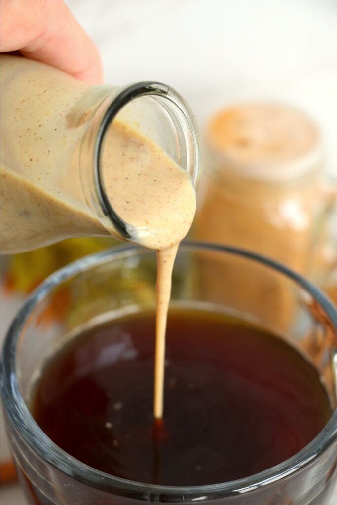 Closeup shot of homemade pumpkin coffee creamer being poured into cup of coffee