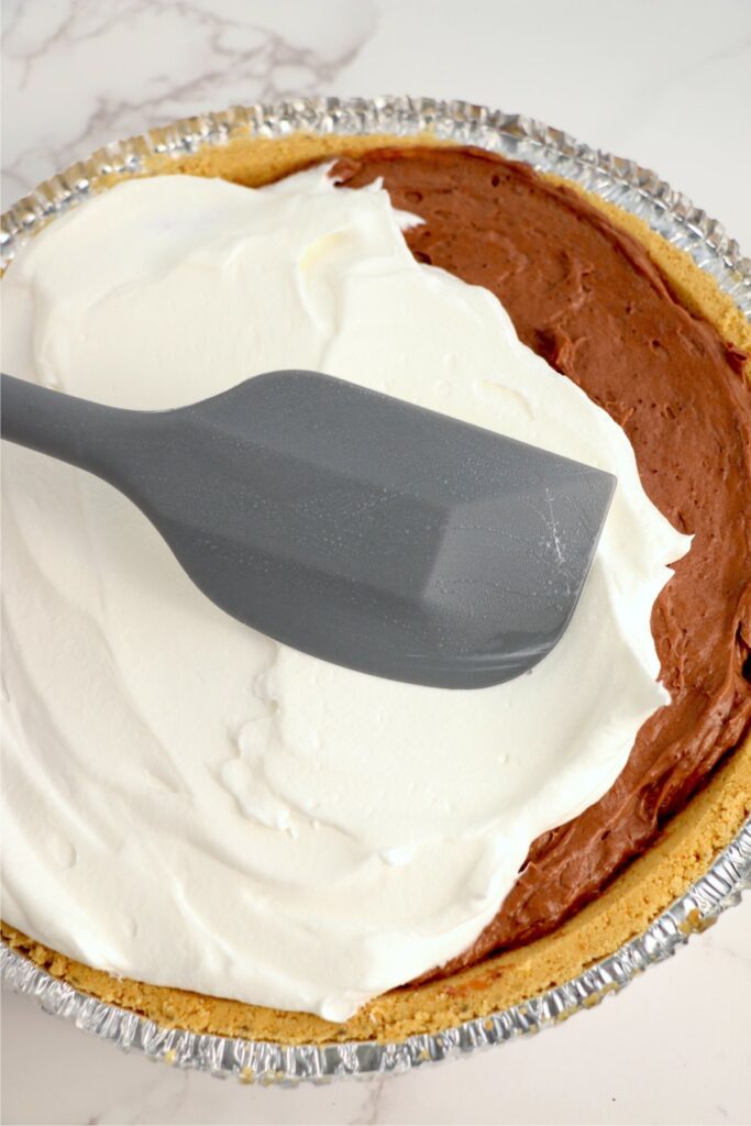 Overehead shot of whipped cream being spread over chocolate pie