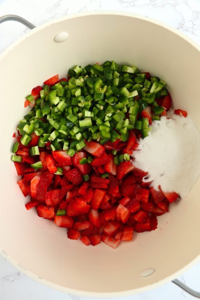 Overhead shot of diced jalapenos and strawberries with sugar in pot