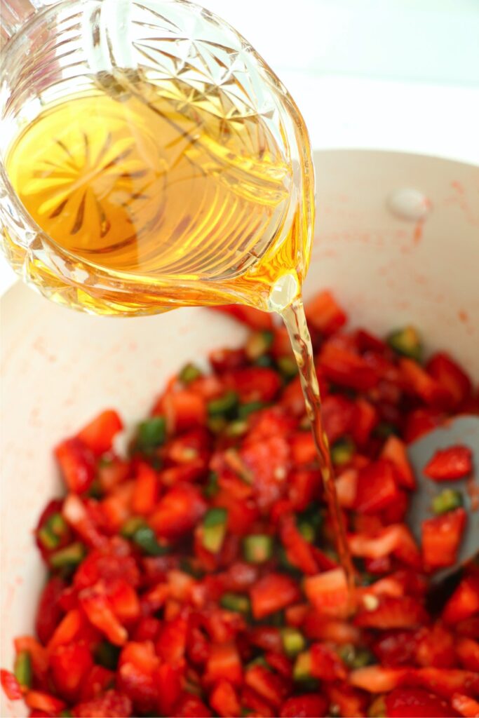 Apple cider vinegar being poured into pot with strawberry jalapeno jam ingredients