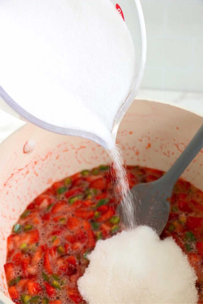 Sugar being poured into strawberry jam in pot