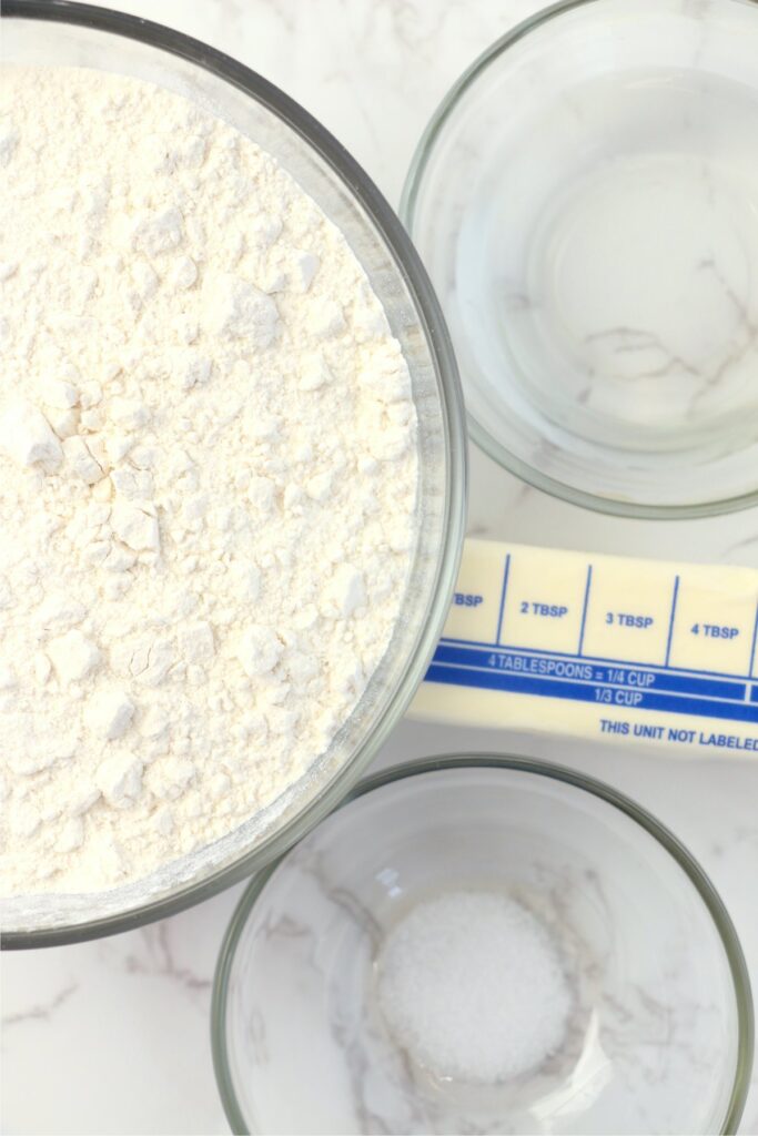 Overheat shot of stick of butter and bowls of flour, slat, and water on table