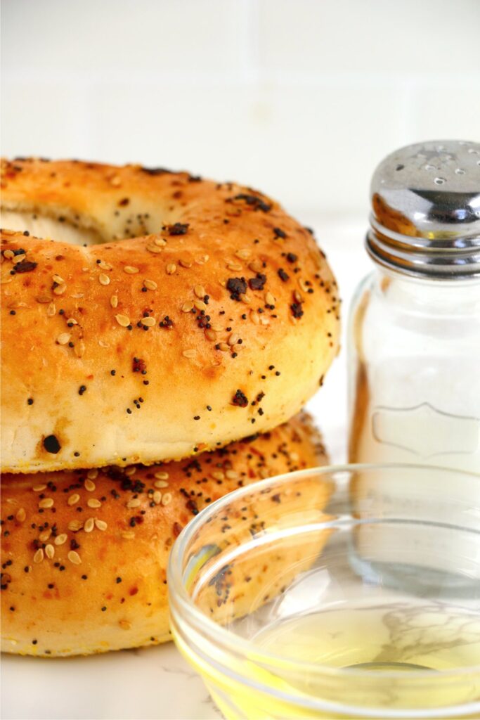 Closeup shot of two bagels stacked atop one another next to bowl of olive oil and salt shaker