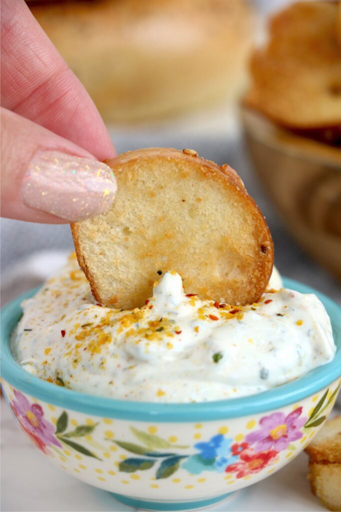 Closeup shot of air fryer bagel chip being dipped into dip