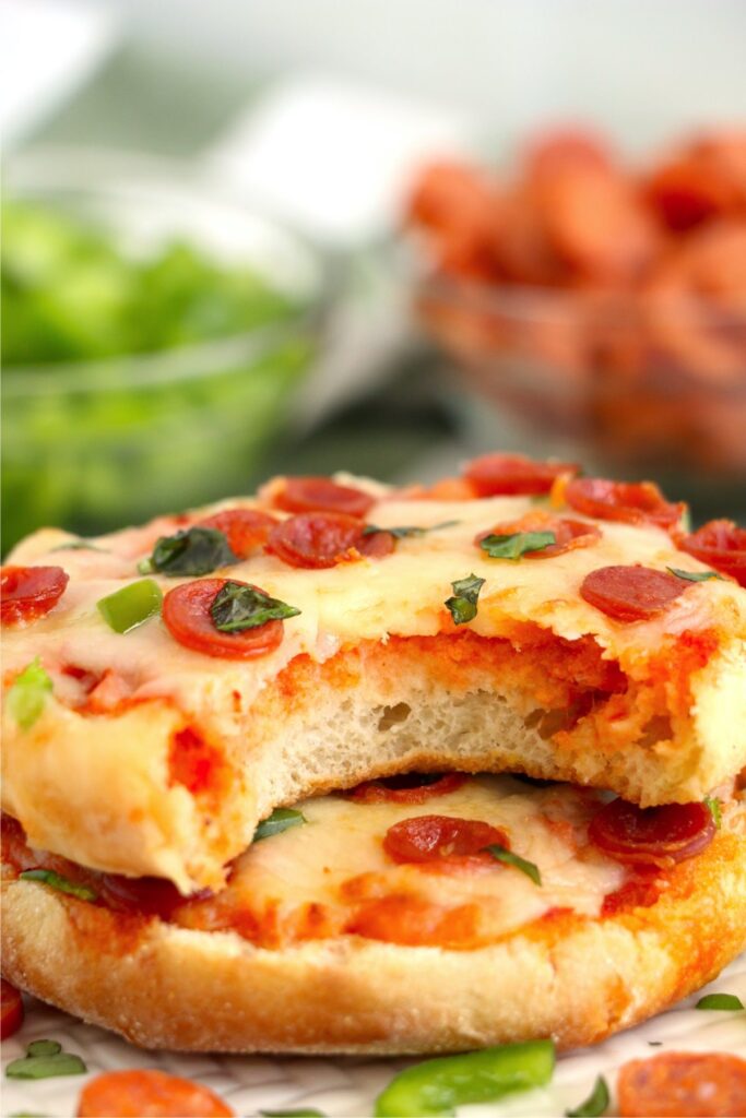  Closeup shot of two air fryer English muffin pizzas stacked atop one another with bite taken out of top pizza