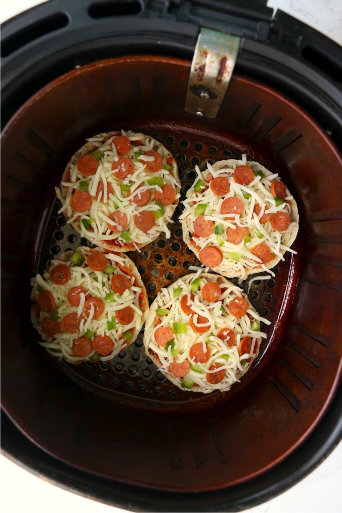 Overhead shot of English muffin pizzas in air fryer basket