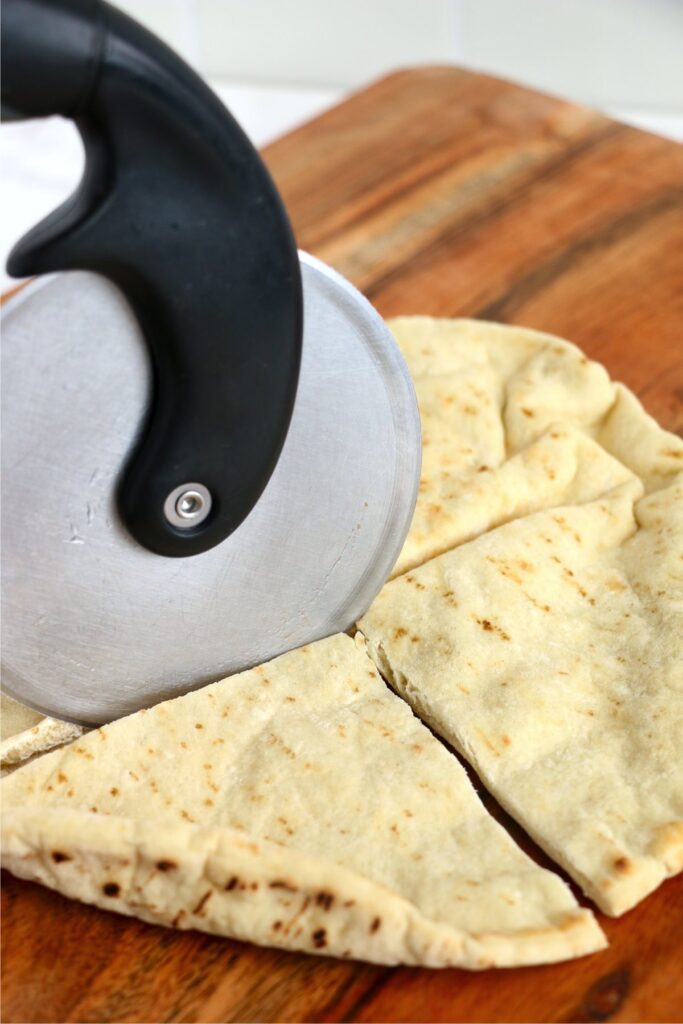 Pizza cutter being used to cut pita into quarters