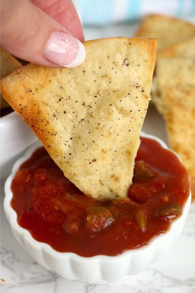 Closeup shot of pita chip being dipped in salsa. 