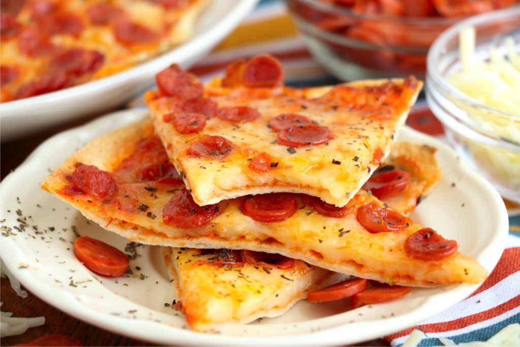 Closeup shot of air fryer tortilla pizza slices on plate with bite taken out of top slice