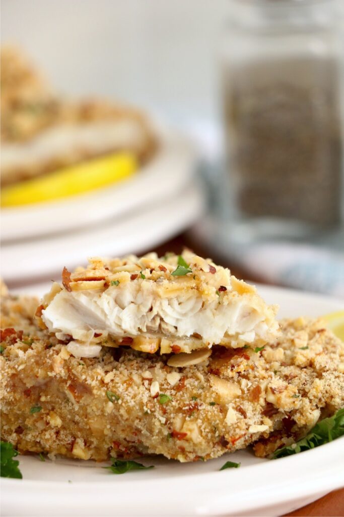 Closeup shot of almond crusted walleye filets stacked atop one another on plate with bite taken out of top filet