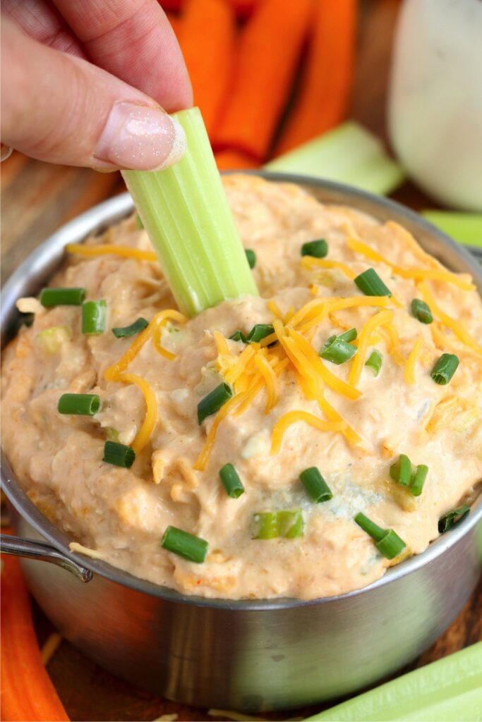 Closeup shot of celery stick being dipped into Buffalo chicken dip