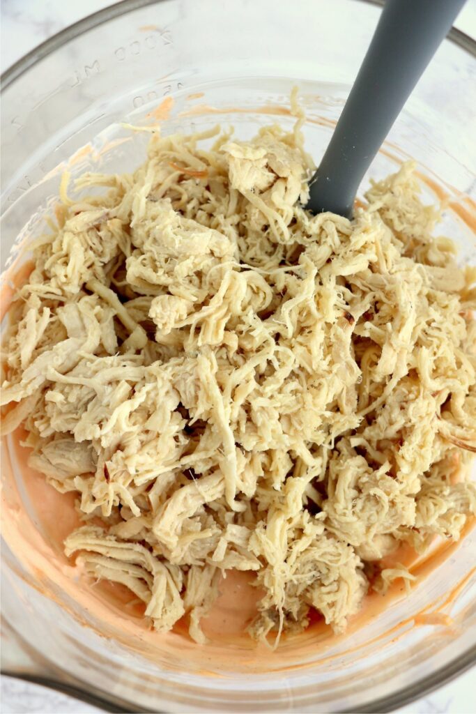 Overhead shot of shredded chicken added to dip ingredients in bowl