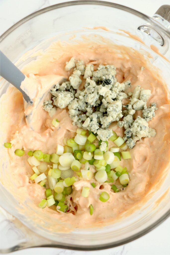 Overhead shot of blue cheese and chopped green onions added to dip