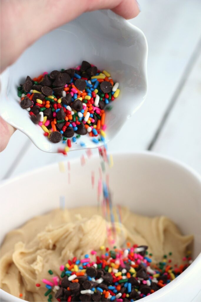 Closeup shot of chocolate chips and sprinkles being poured into bowl of cookie dough dip