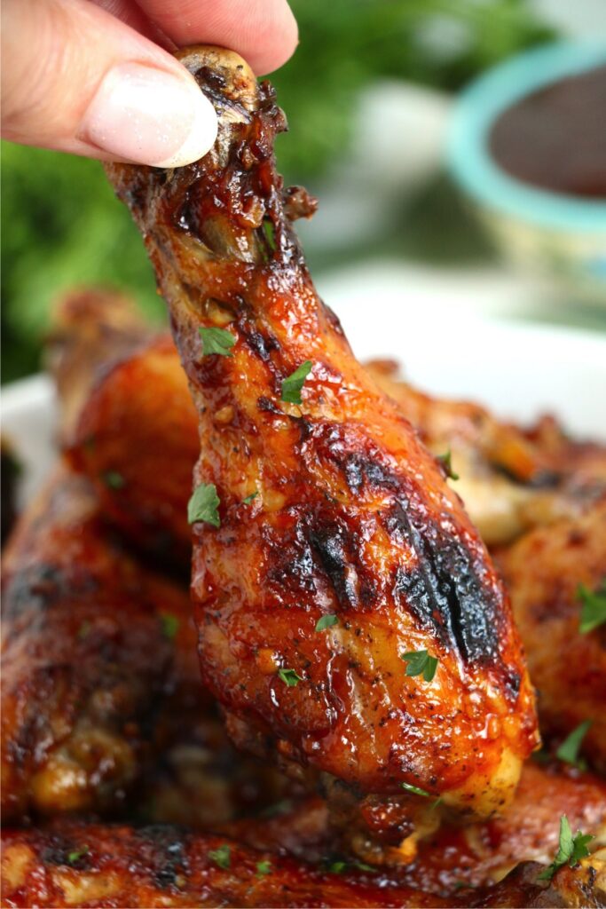 Closeup shot of hand holding crock pot BBQ chicken drumstick over more drumsticks