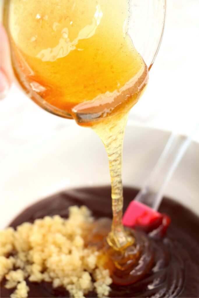 Honey being poured into mixing bowl with bbq sauce and brown sugar