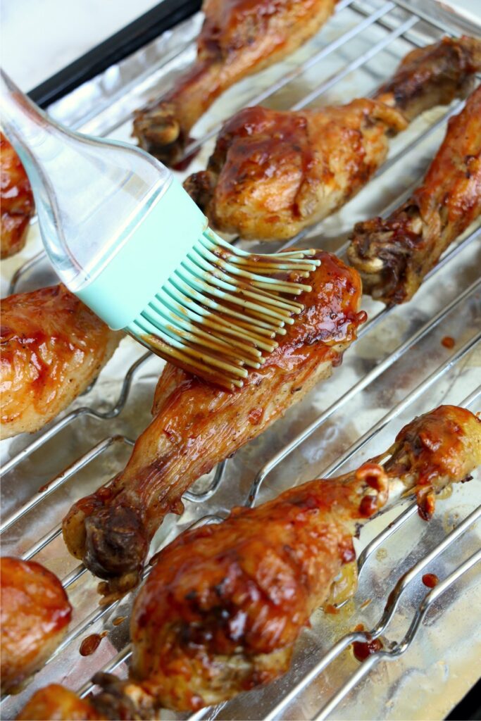 Overhead shot of bbq sauce being brushed onto chicken drumsticks