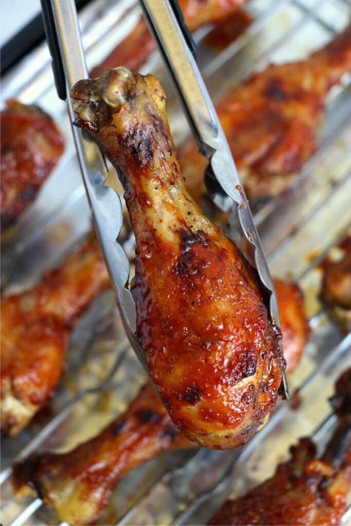 Closeup shot of tongs holding a crock pot bbq chicken drumstick