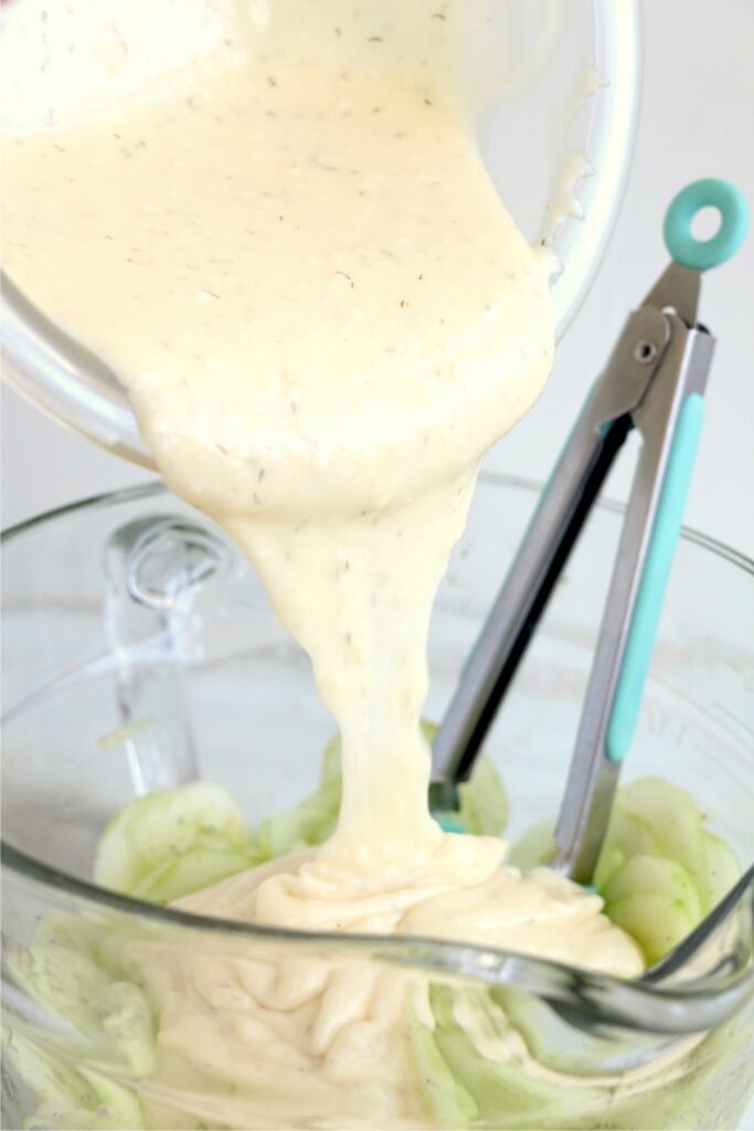 Dressing being poured over sliced cucumbers in bowl