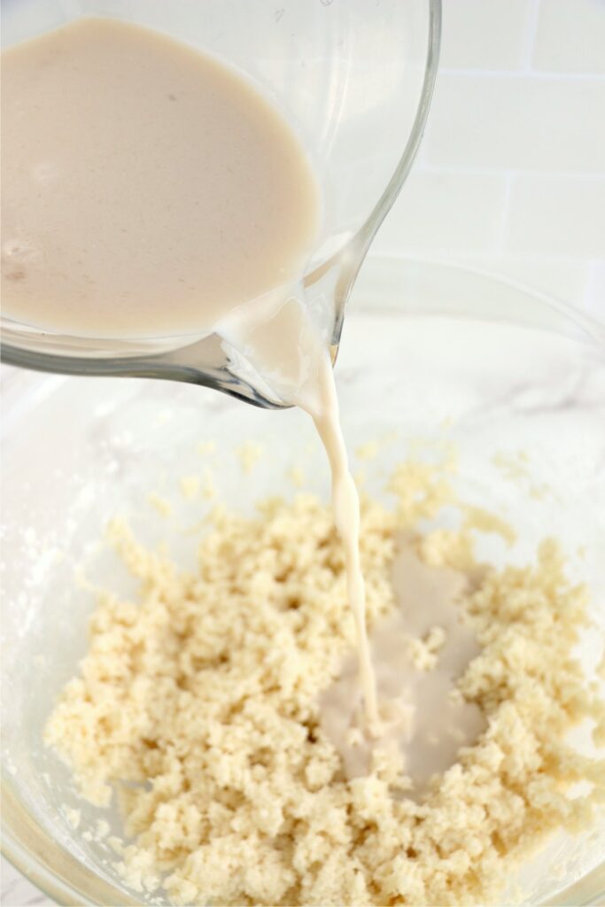 Wet cake ingredients being poured into bowl of dry ingredients