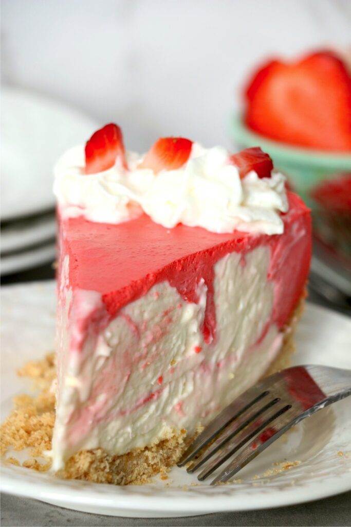 Closeup shot of slice of no bake strawberry jello cheesecake on plate with fork