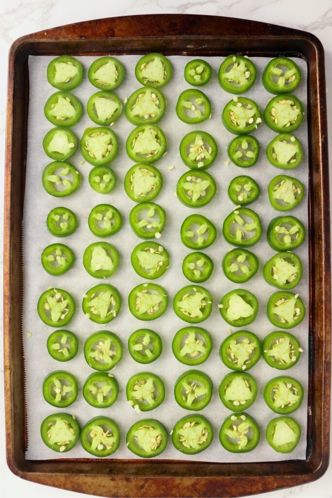 Overhead shot of sliced jalapenos on baking sheet lined with parchment paper