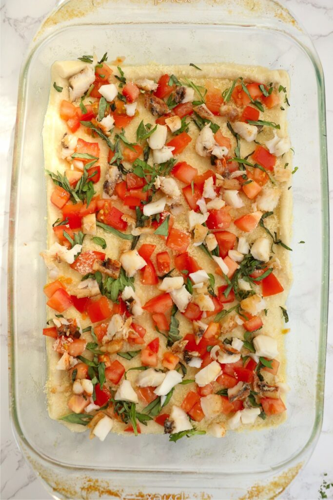 Overhead shot of lobster, tomatoes, and basil on pizza dough