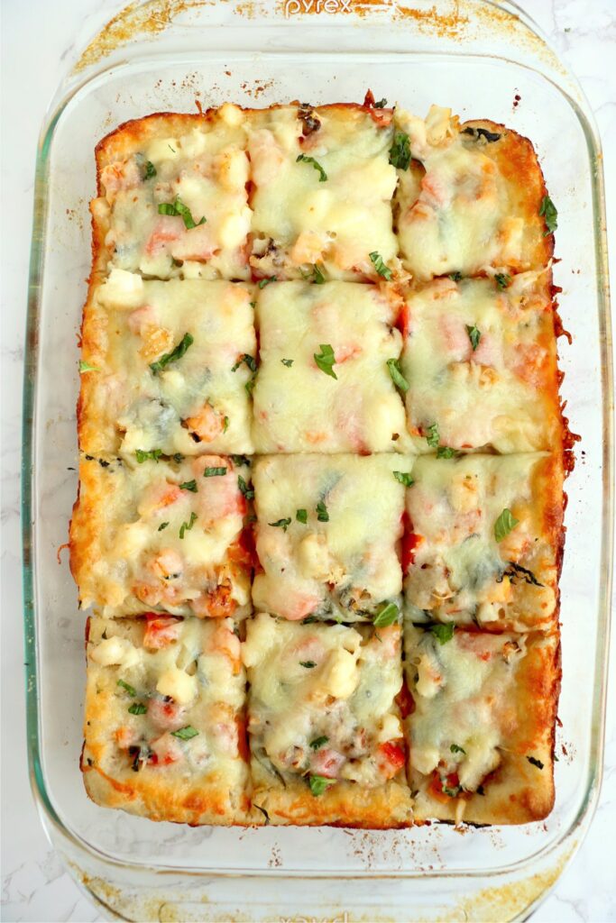 Overhead shot or Red Lobster lobster pizza cut into slices in baking dish