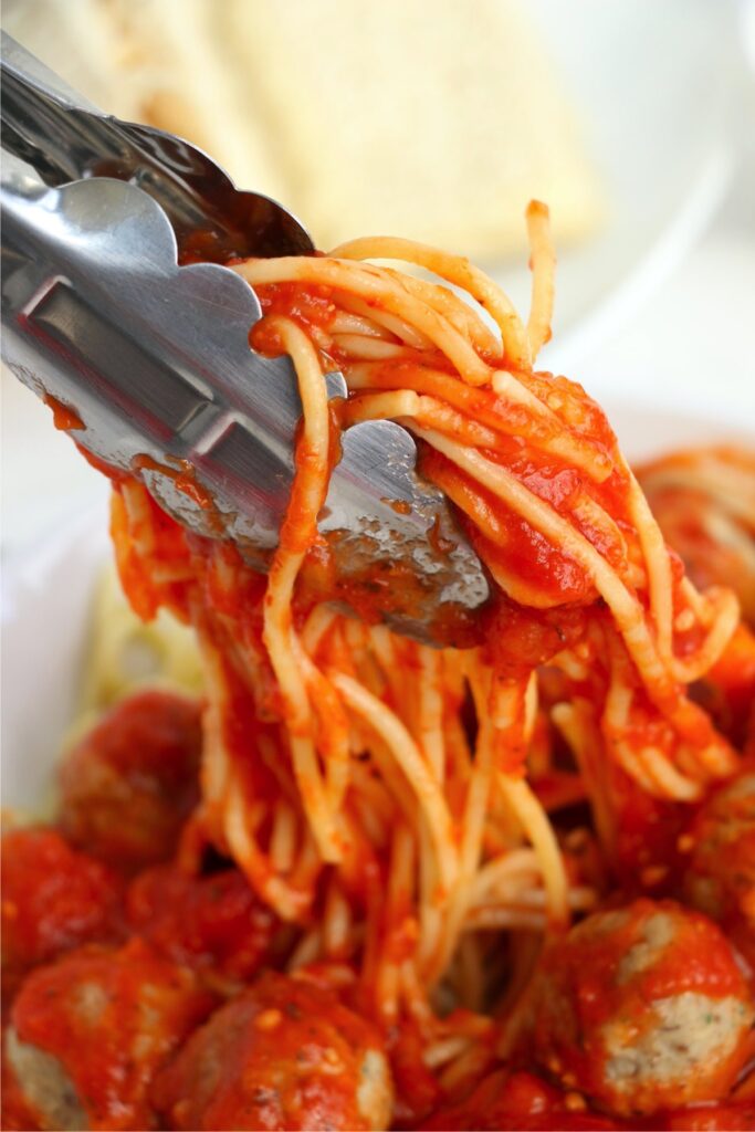 Closeup shot of tongs holding spaghetti and meatballs