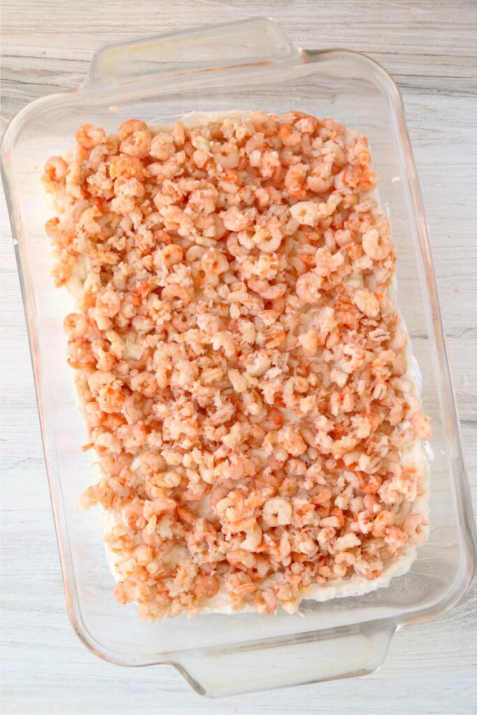 Overhead shot of shrimp sprinkled over cream cheese base spread in baking dish