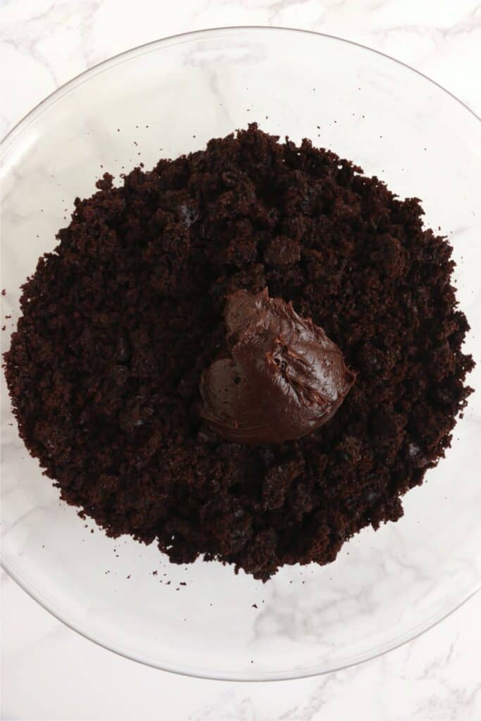 Overhead shot of crumbled chocolate cake and chocolate frosting in mixing bowl