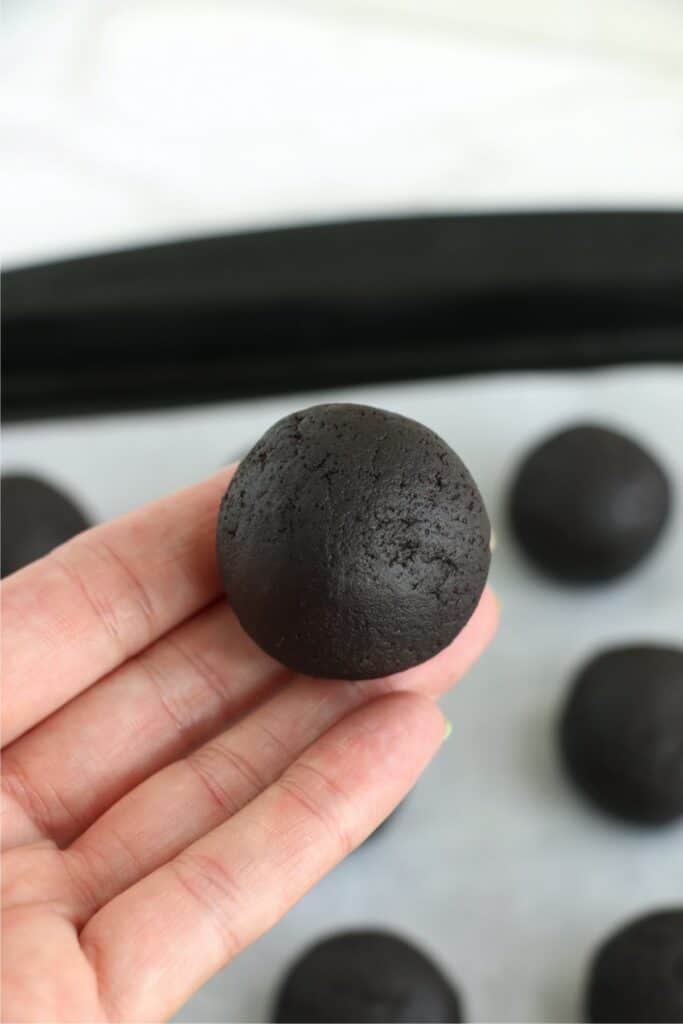 Closeup shot of hand holding a cake ball over a baking sheet with more cake balls