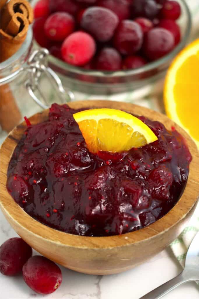 Closeup shot of bowlful of cranberry sauce with cinnamons sticks and cranberries in background