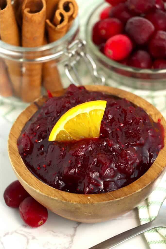 Bowlful of instant pot cranberry sauce next to jar of cinnamon sticks and bowl of cranberries