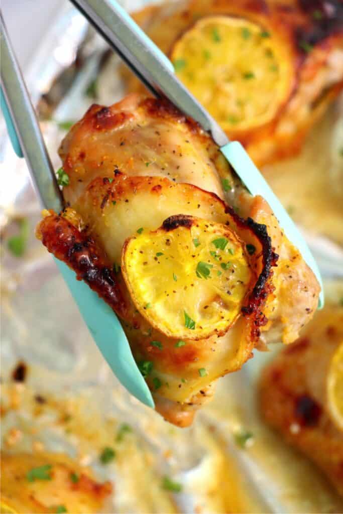 Closeup shot of tongs holding a honey garlic lemon pepper chicken thigh over a dish of more chicken thighs