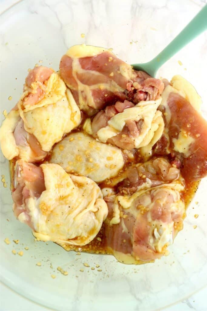 Overhead shot of chicken thighs mixed with honey garlic lemon pepper mixture in mixing bowl