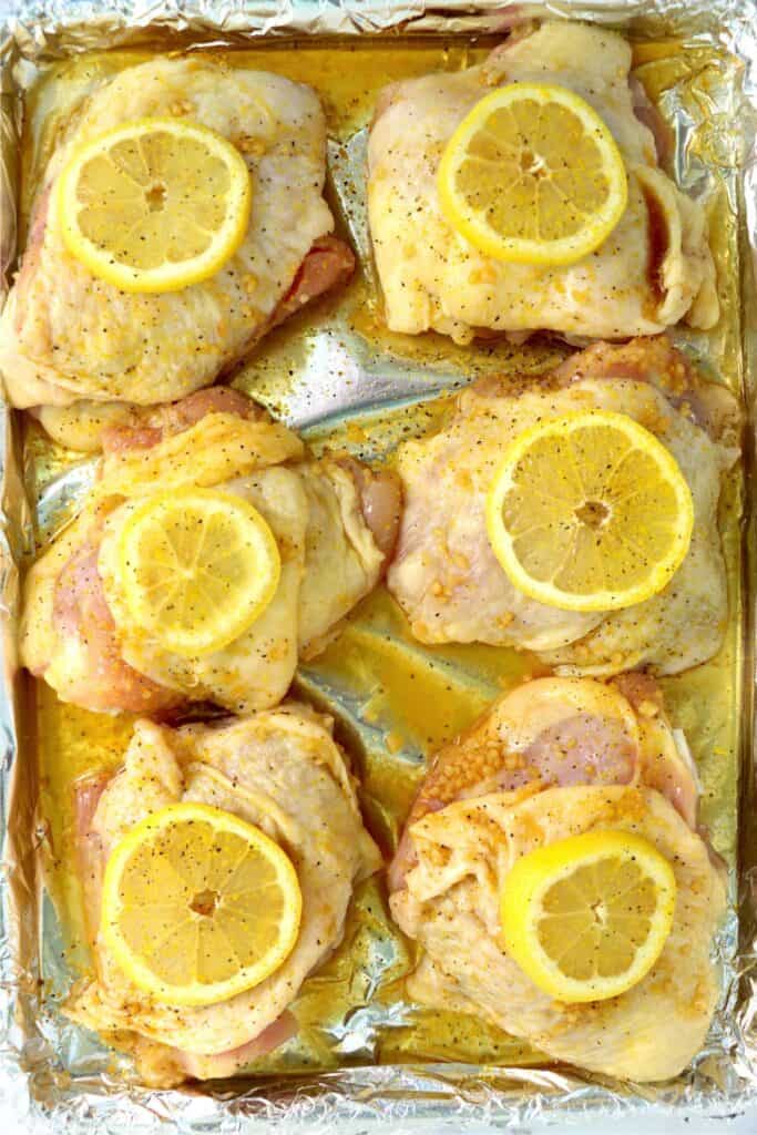 Overhead shot of honey garlic lemon pepper chicken thighs topped with lemon slices on baking sheet