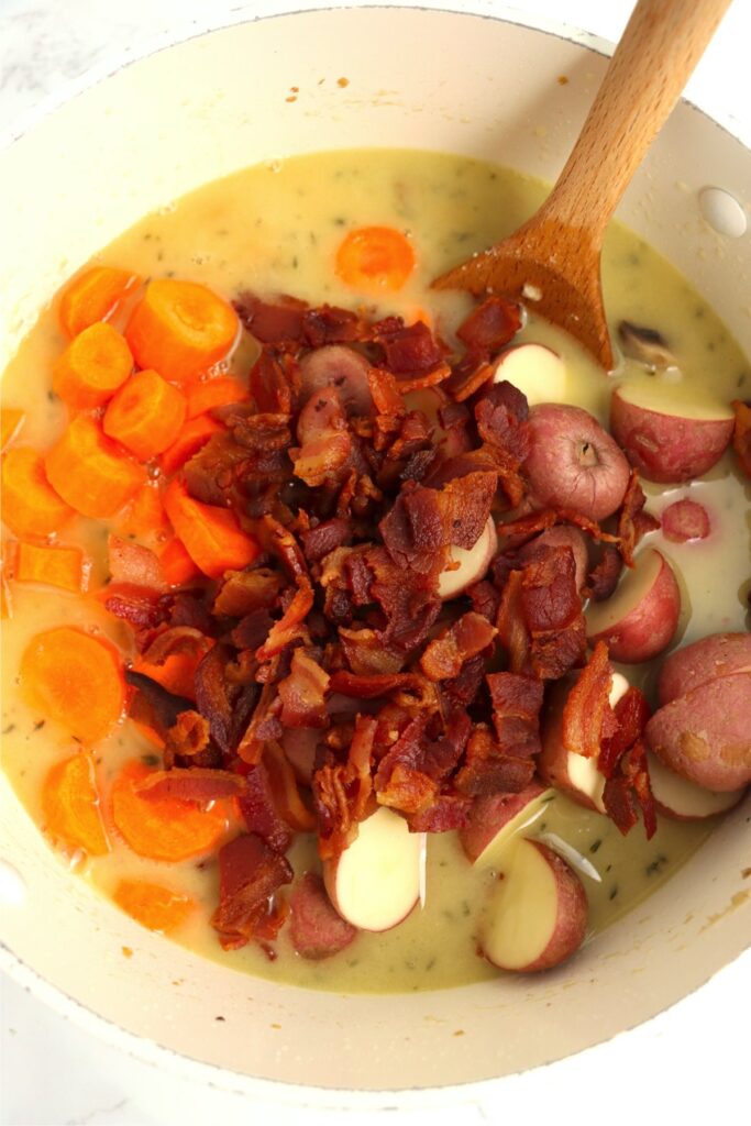 Overhead shot of bacon, potatoes, and carrots in pot of soup.